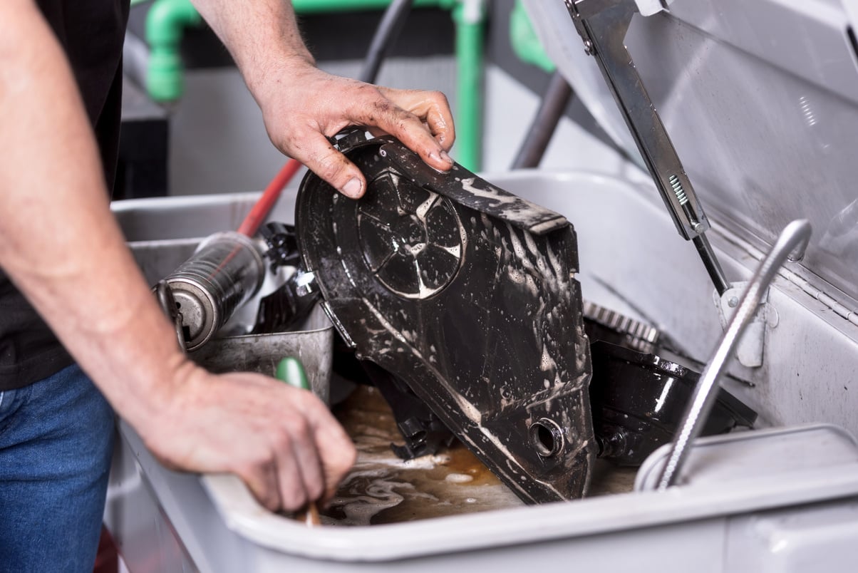 Mechanic degreasing a car engine part at service repair station.